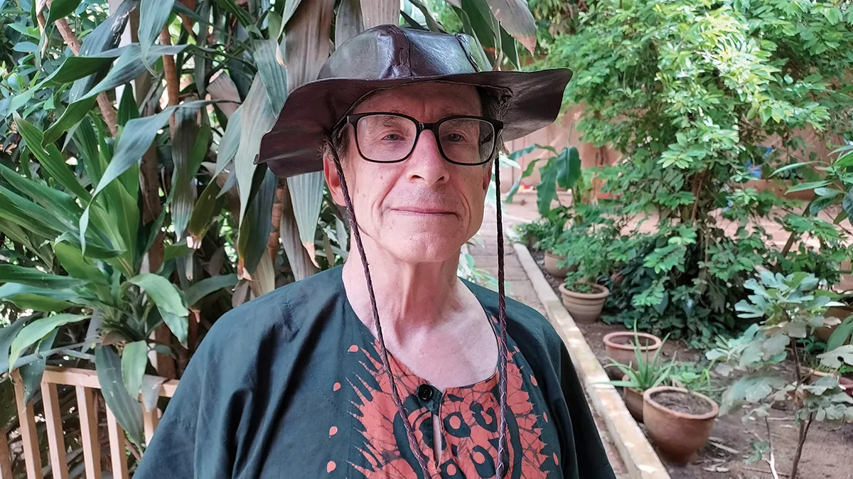 Bill Miles in front of plants and trees with bucket hat on
