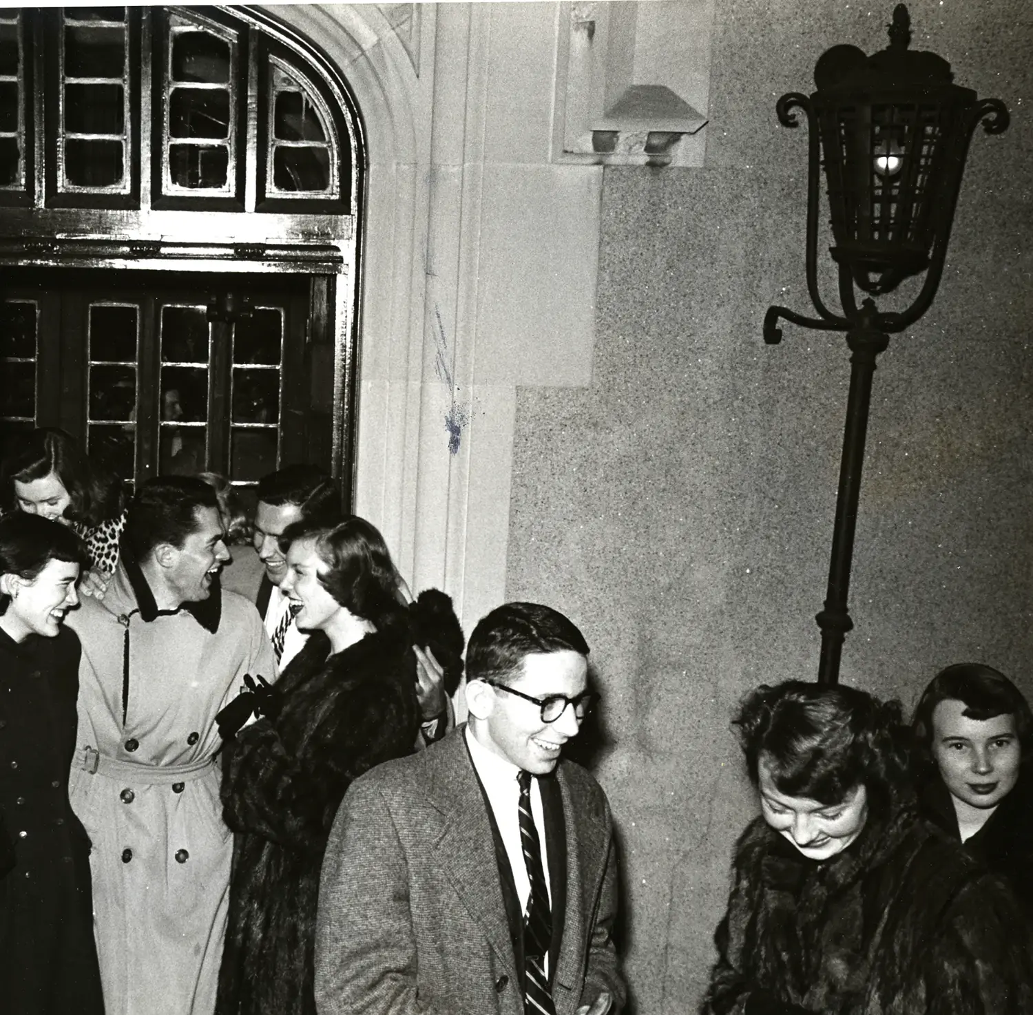 Old black and white photograph of students smiling and laughing outside the doors