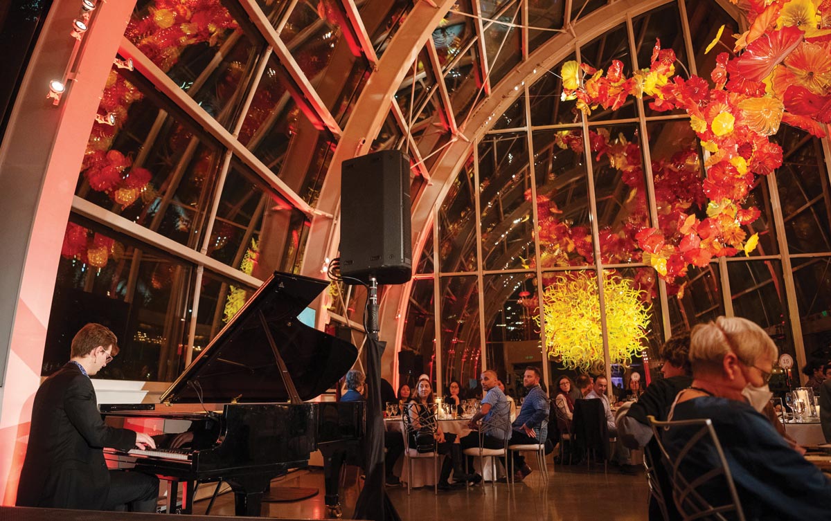 During dinner, a man plays a grand piano in the glass atrium of the Chihuly Garden and Glass, surrounded by Dale Chihuly’s colorful sculptural works.