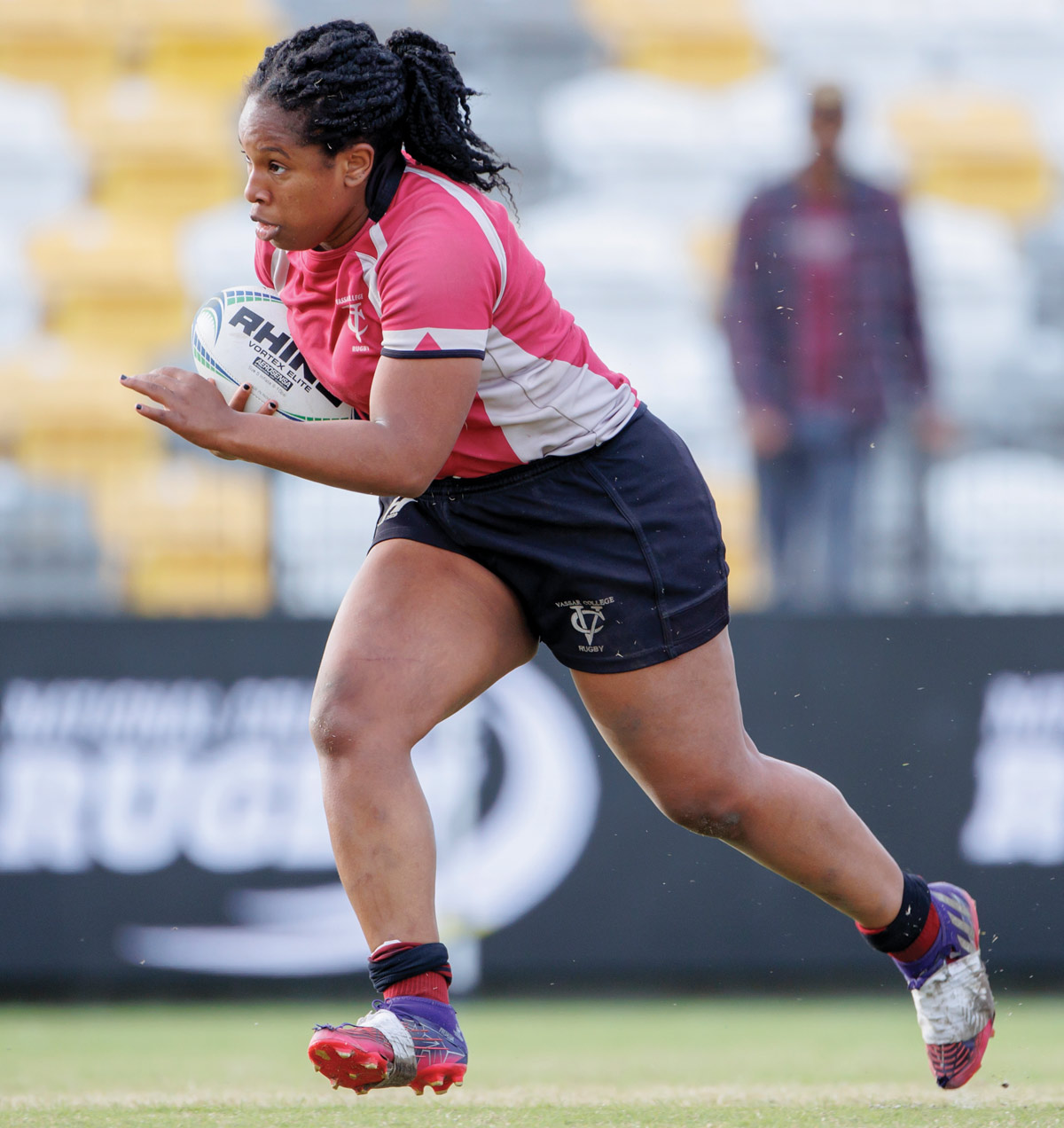 A women’s rugby player sprints across the field with a ball.