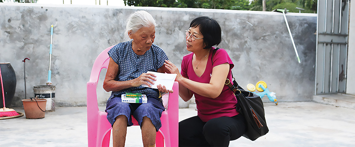 Professor Qiu kneels down to speak with aging survivor Chen Liancun.