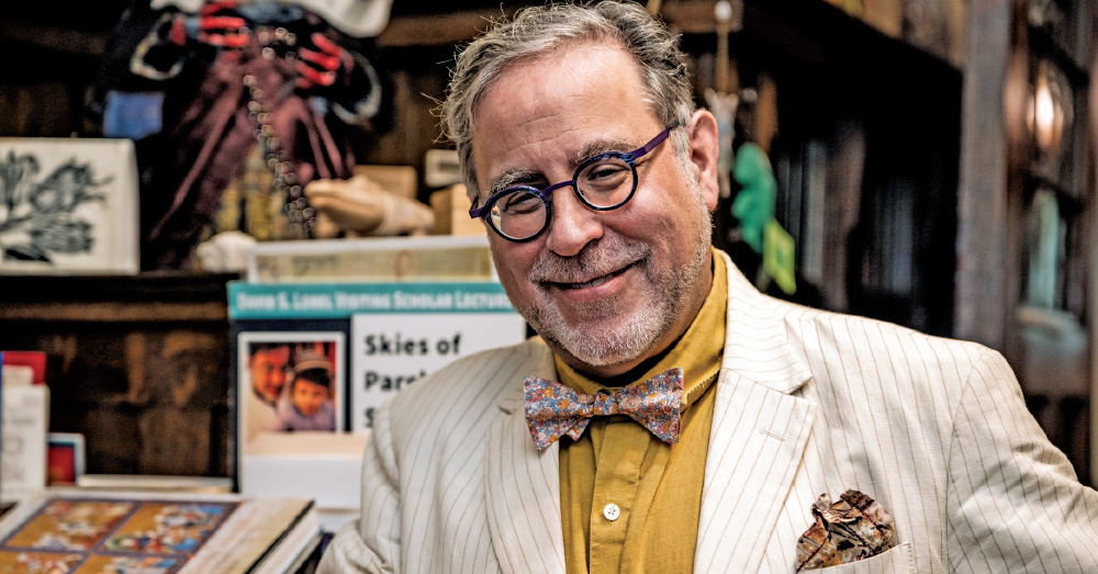 Mark Michael Epstein, professor of religion, smiling while wearing a yellow shirt, white striped blazer, and floral bow tie.