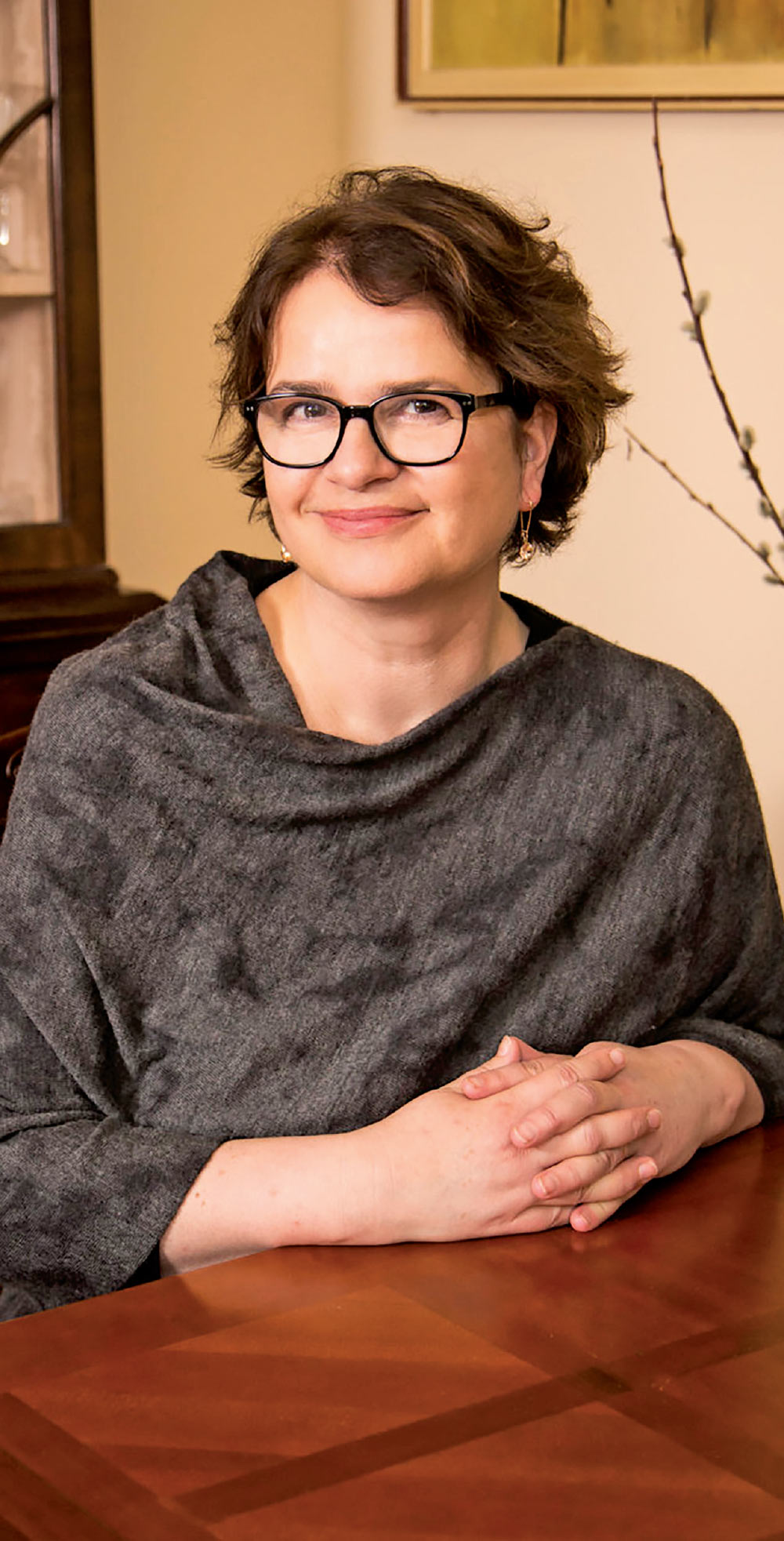 Paulina Bren seated at a wooden table wearing a grey shawl.