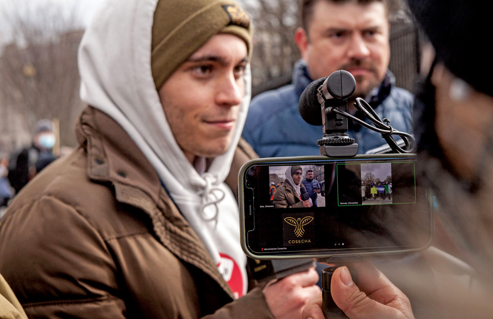 Carlos Espina, in white hoodie and brown jacket, is videotaped  by reporters during a protest at the White House.