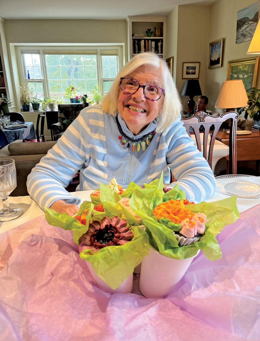 Marianne Heath Mundy (’51) smiles broadly, seated at a table with flowers in front of her.