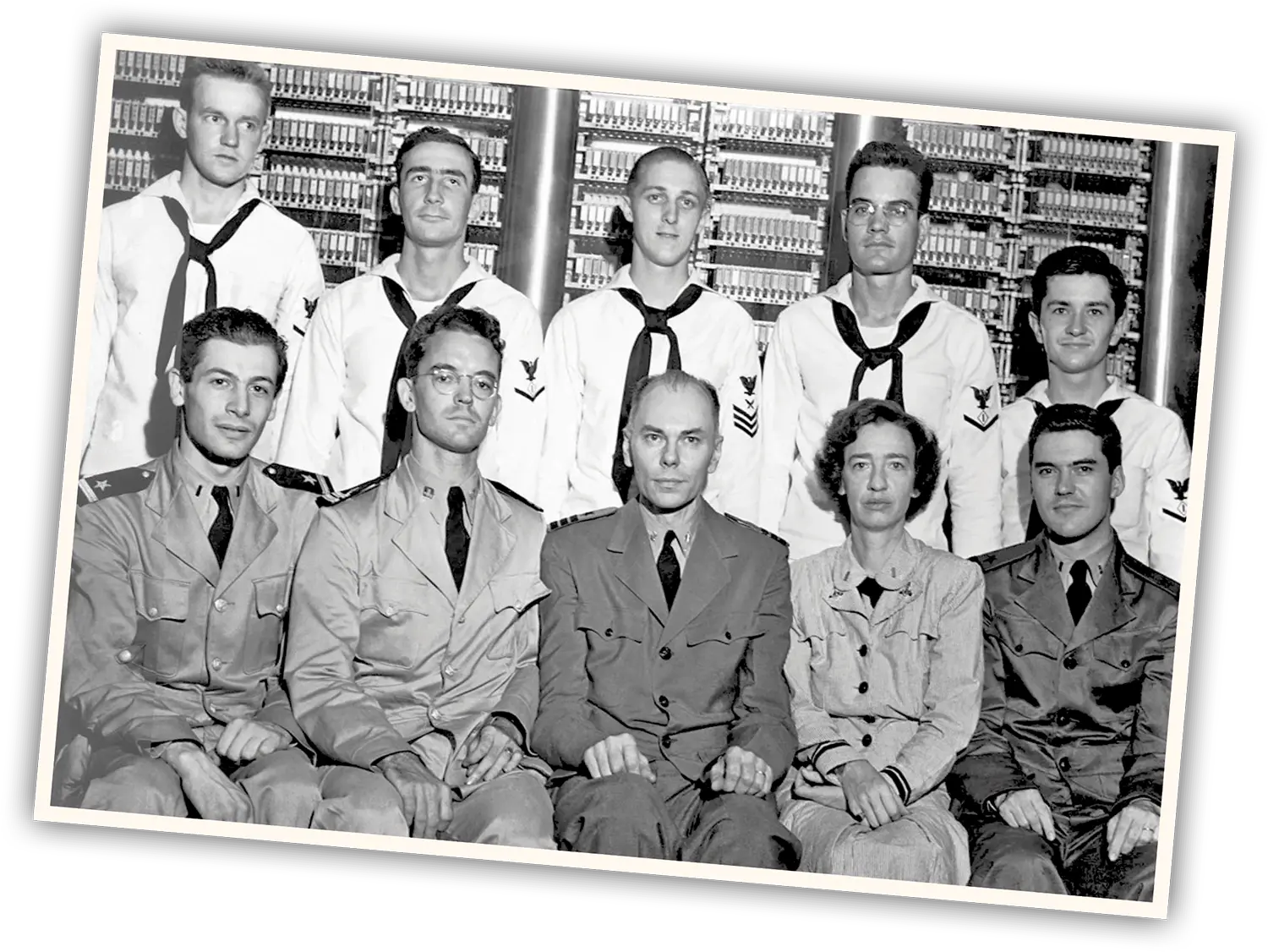 A black and white photograph of ten individuals in military and naval uniforms, posed in front of early computer equipment.