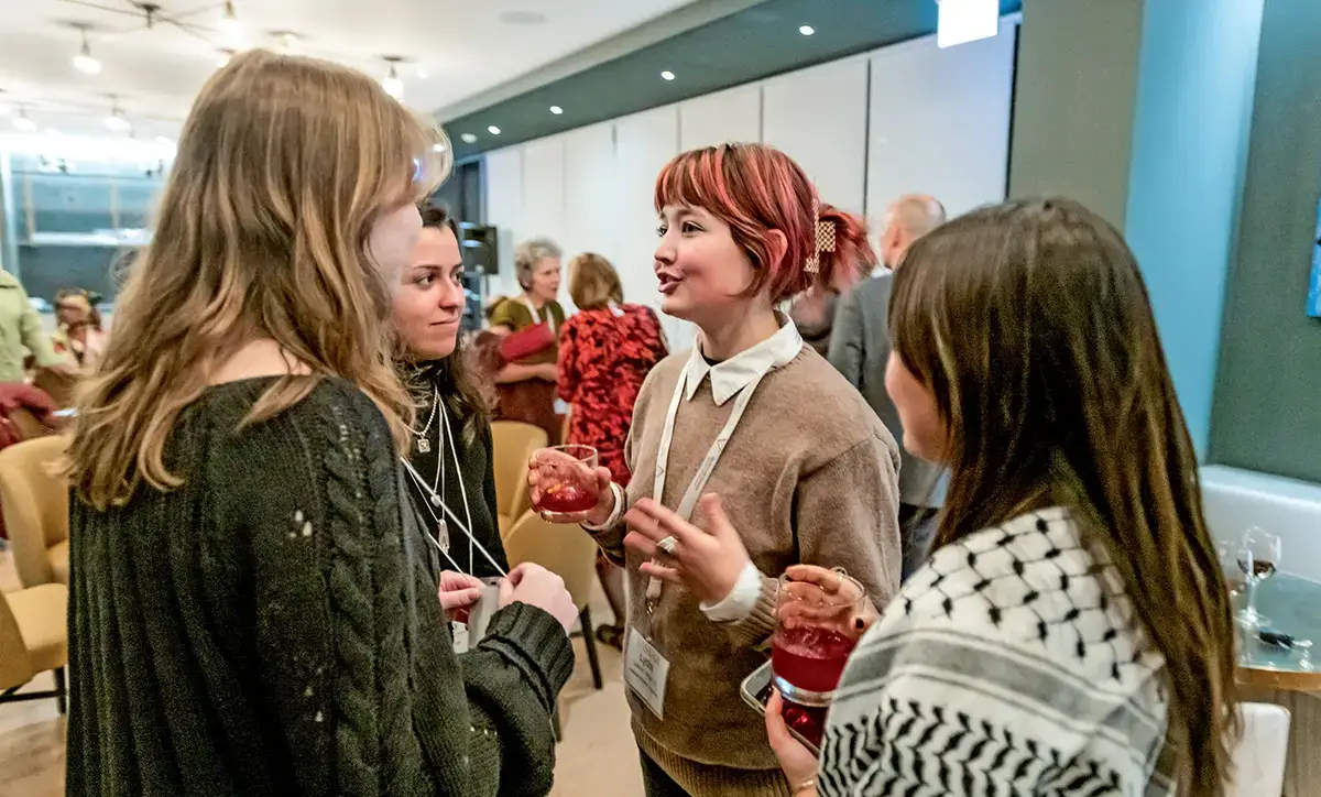 Four young women stand in a circle conversing during a reception at the restaurant bar. 