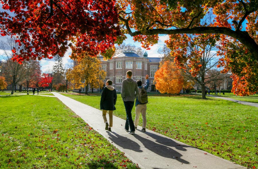 Students walk on the quad towards Rockefeller Hall as trees turn orange and red for fall.