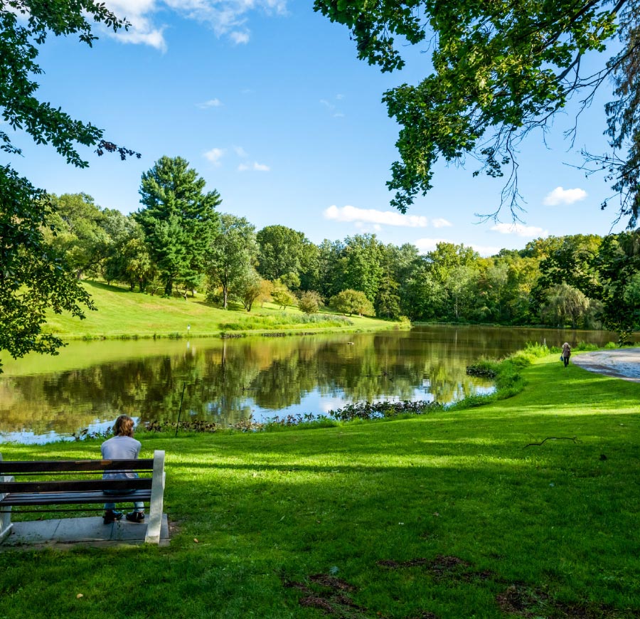 A student sit contemplatively on a bench looking out at Sunset Lake.