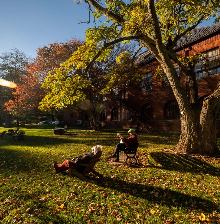 An older couple sits on benches and chairs outside of Ely Hall.