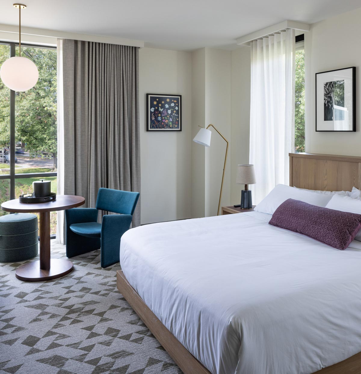 A well-appointed hotel room with a large bed, art on the walls, and a large floor-to-ceiling window with outdoor vistas.