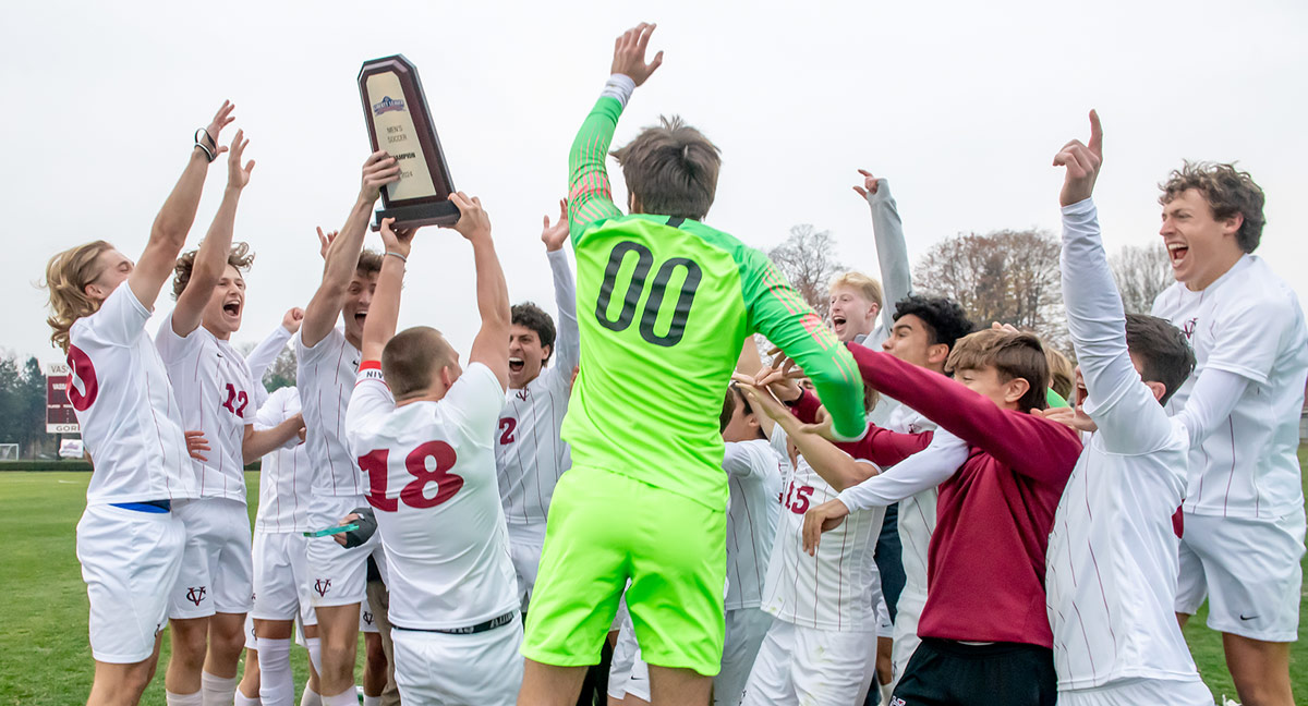 Vassar Men’s Soccer team celebrates winning the Liberty League Championship while holding trophy and jumping.