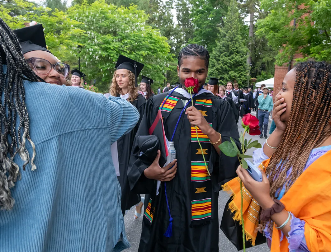 A graduate smells a rose given to him by a woman.