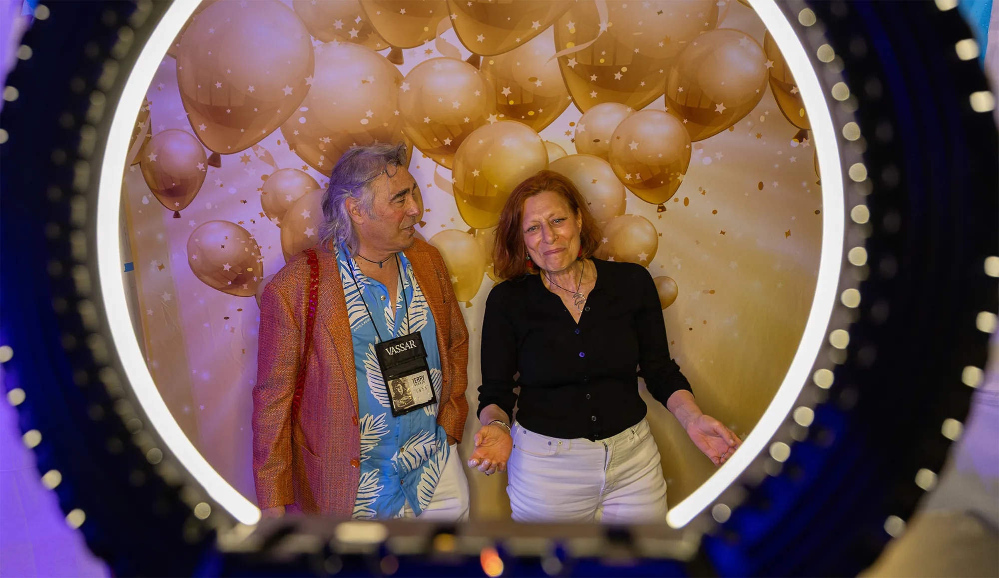 Two joyous alums pose in a photo booth with festive balloon shapes in the background.