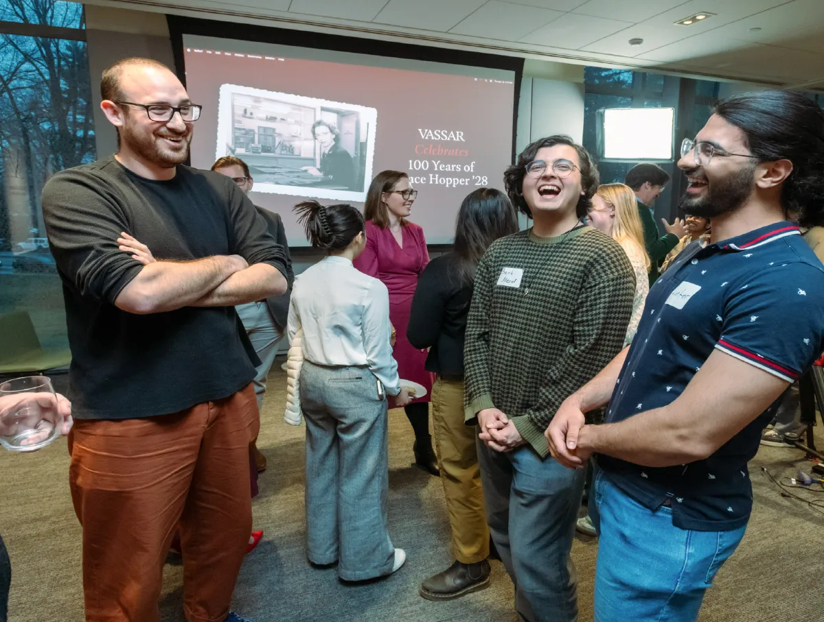 Vassar students and alums share a jovial moment with a Grace Hopper Day image behind them.