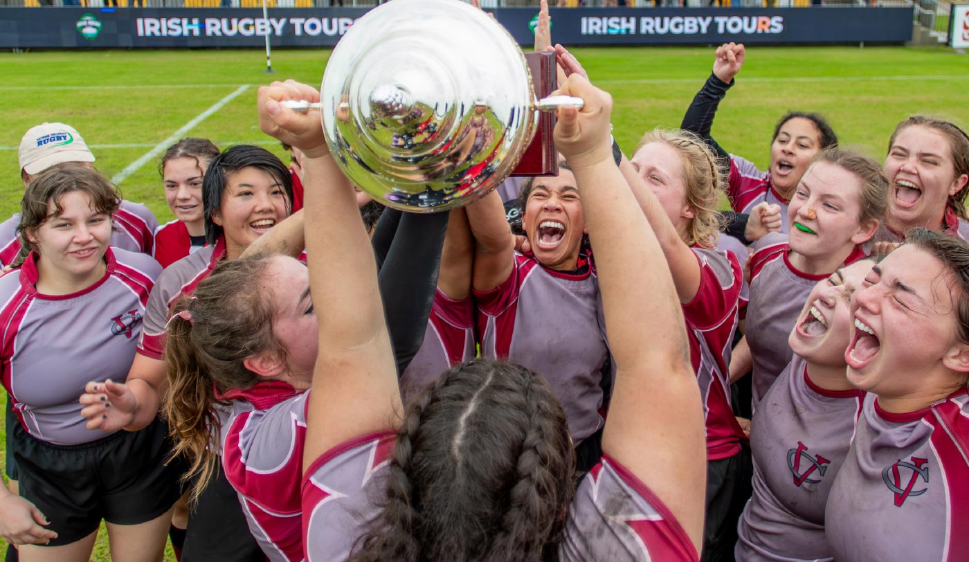 The Vassar Women’s Rugby team huddles and celebrates around a trophy.