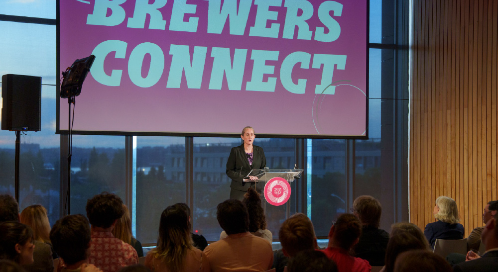 Michelle Walsh addresses an audience. A slide  behind her reads “Brewers Connect.”