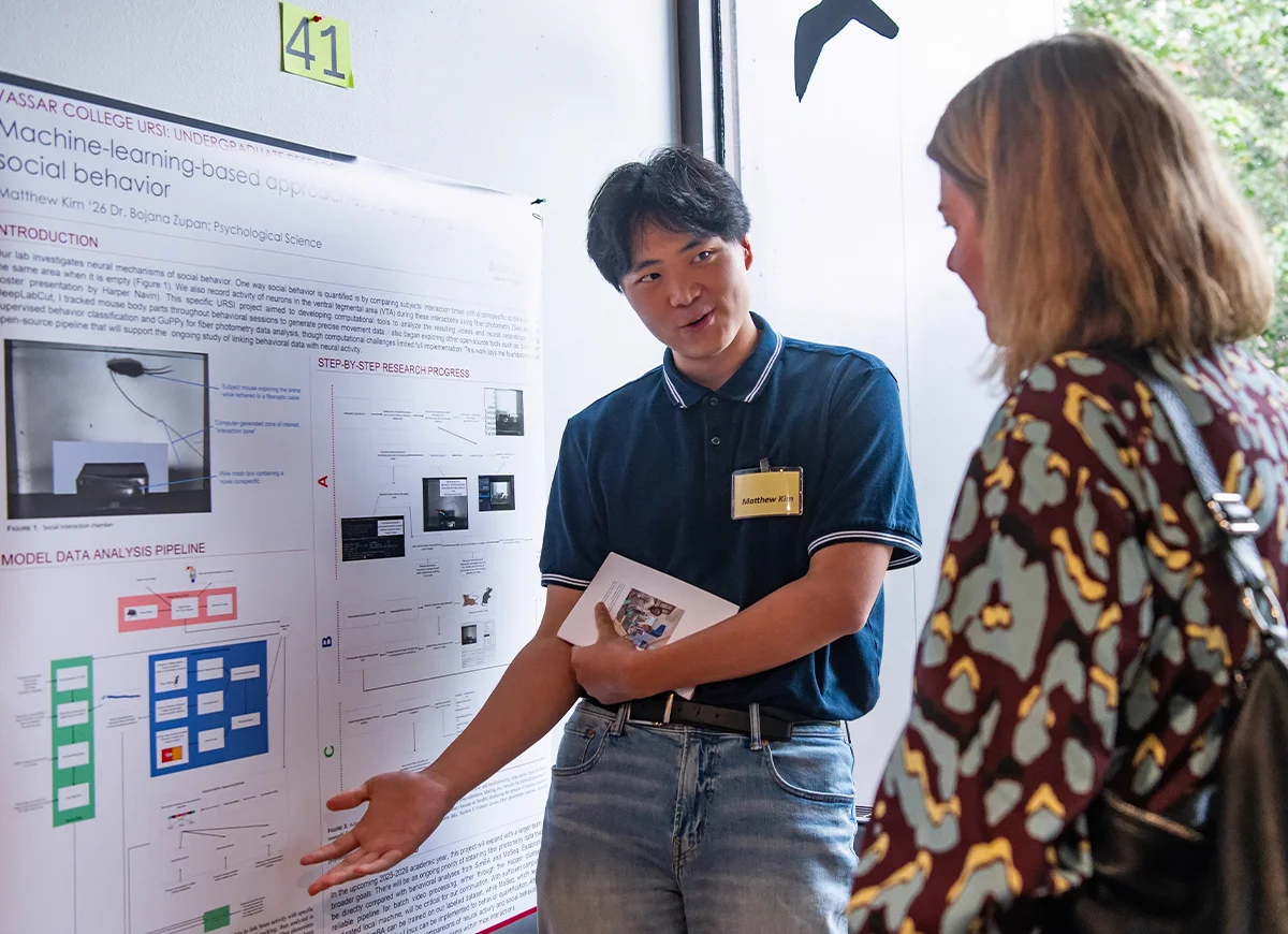 Student explains his research in front of a presentation poster.