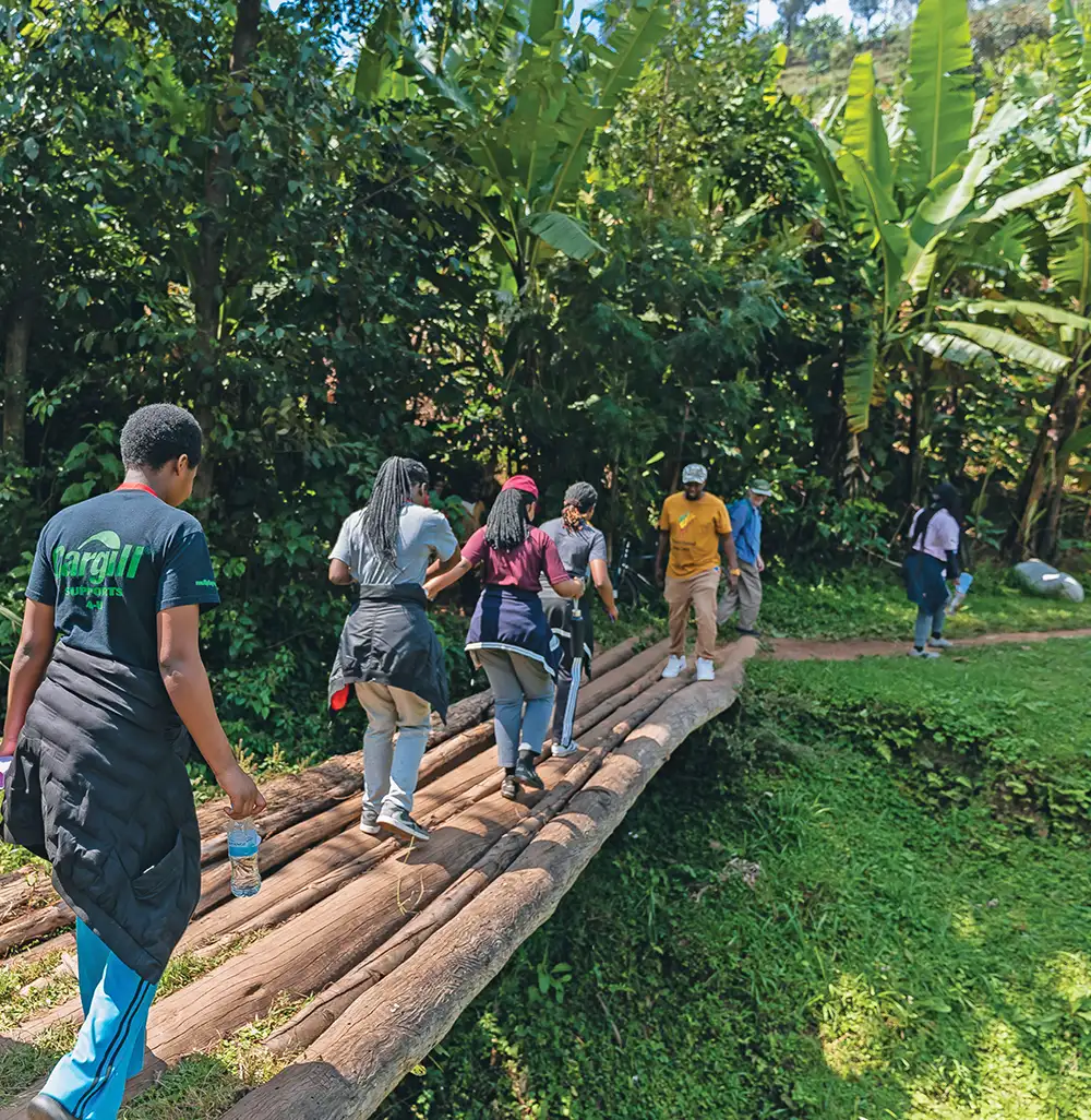 Students and Professors following along a wooden bridge in Rwanda, made of three thin logs.