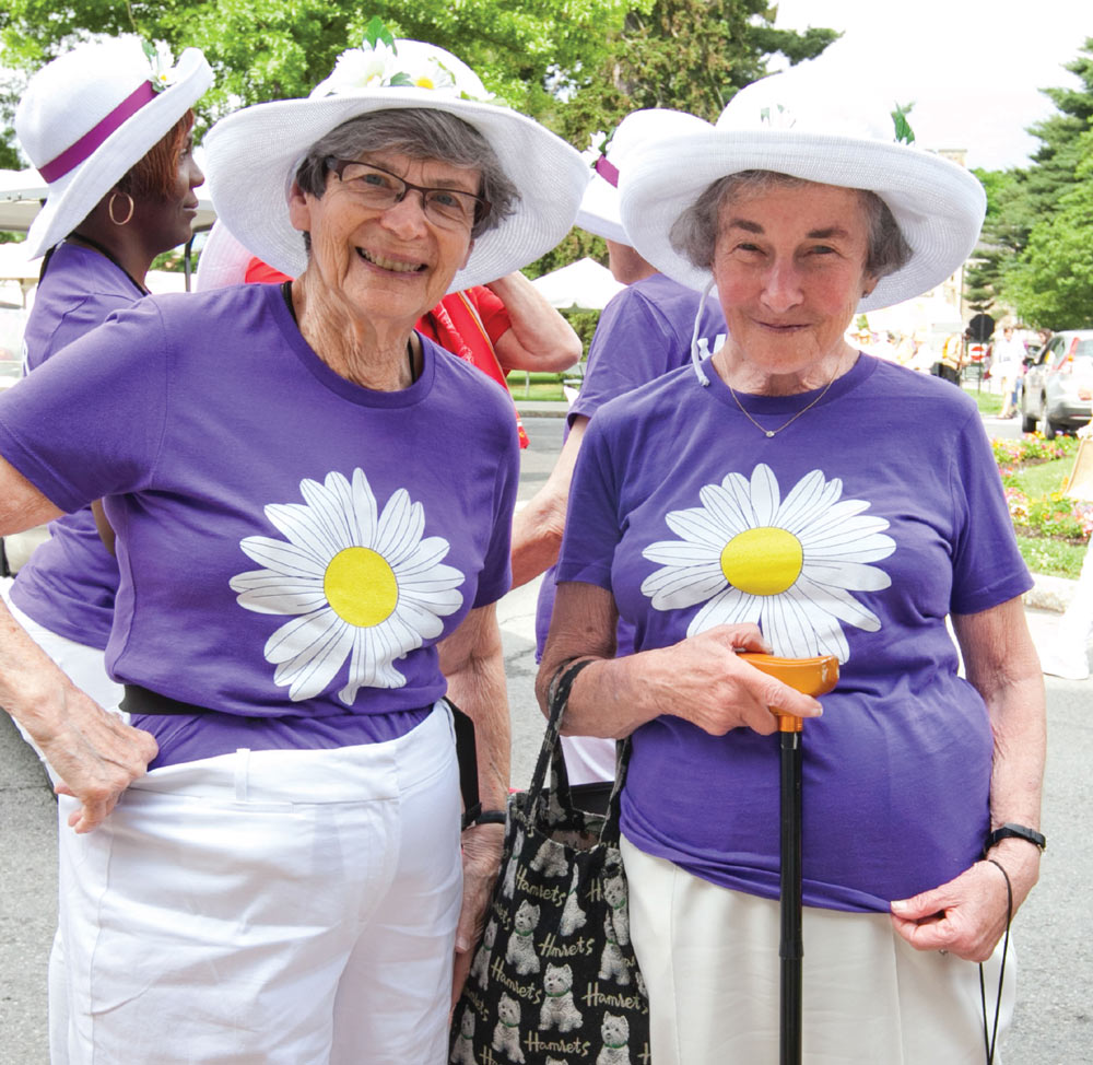 June Marks ‘49 standing with a friend at Vassar’s 2014 reunion, both wear purple shirts each emblazoned with a large white daisy on it.