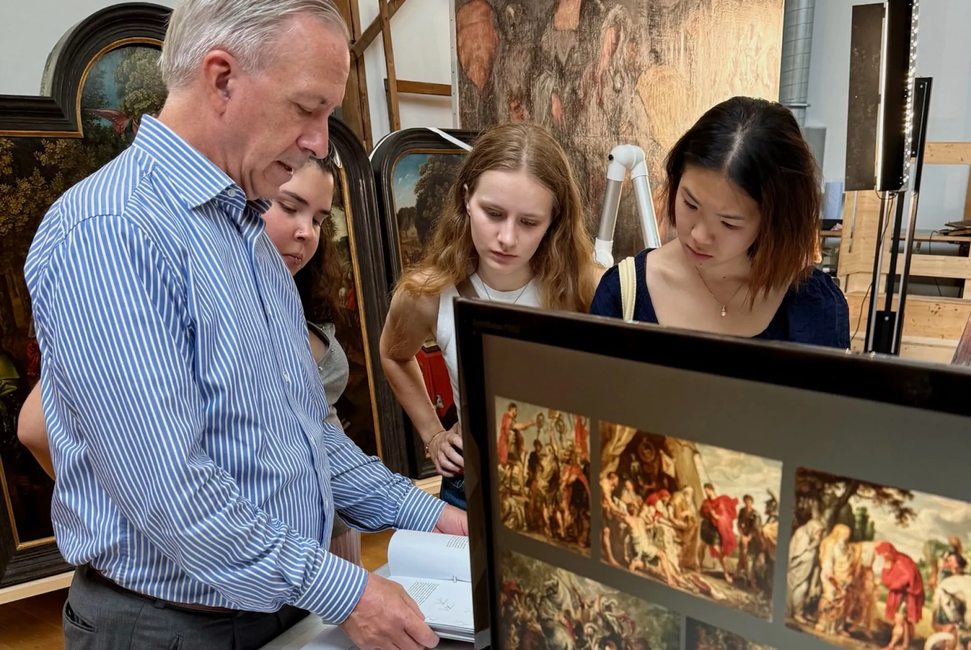 Kathleen Chang, Betsy Subiros, and Emma Larson—all ‘25—speaking with an art museum curator as he shows them a book normally unavailable for public viewing.