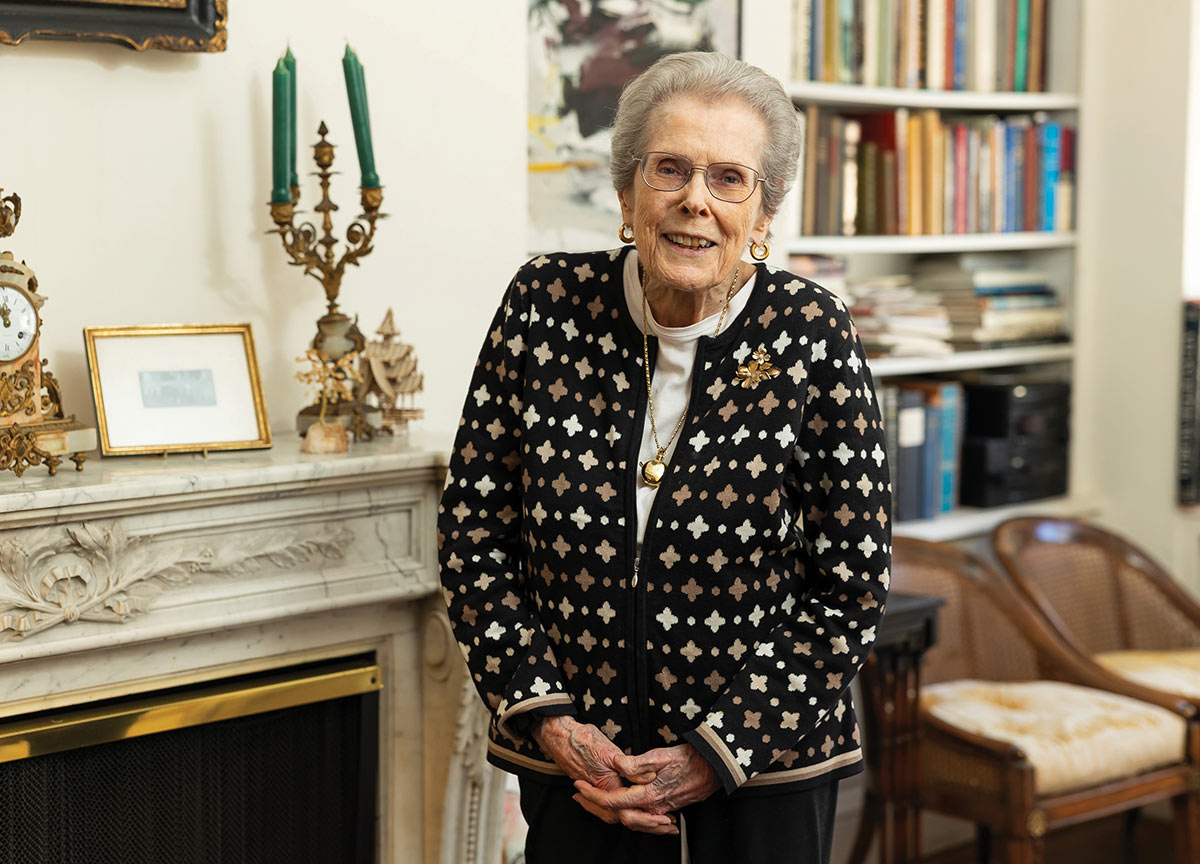 Mary C. Schlosser standing in a room with a bookshelf in the background and a marble fireplace beside her