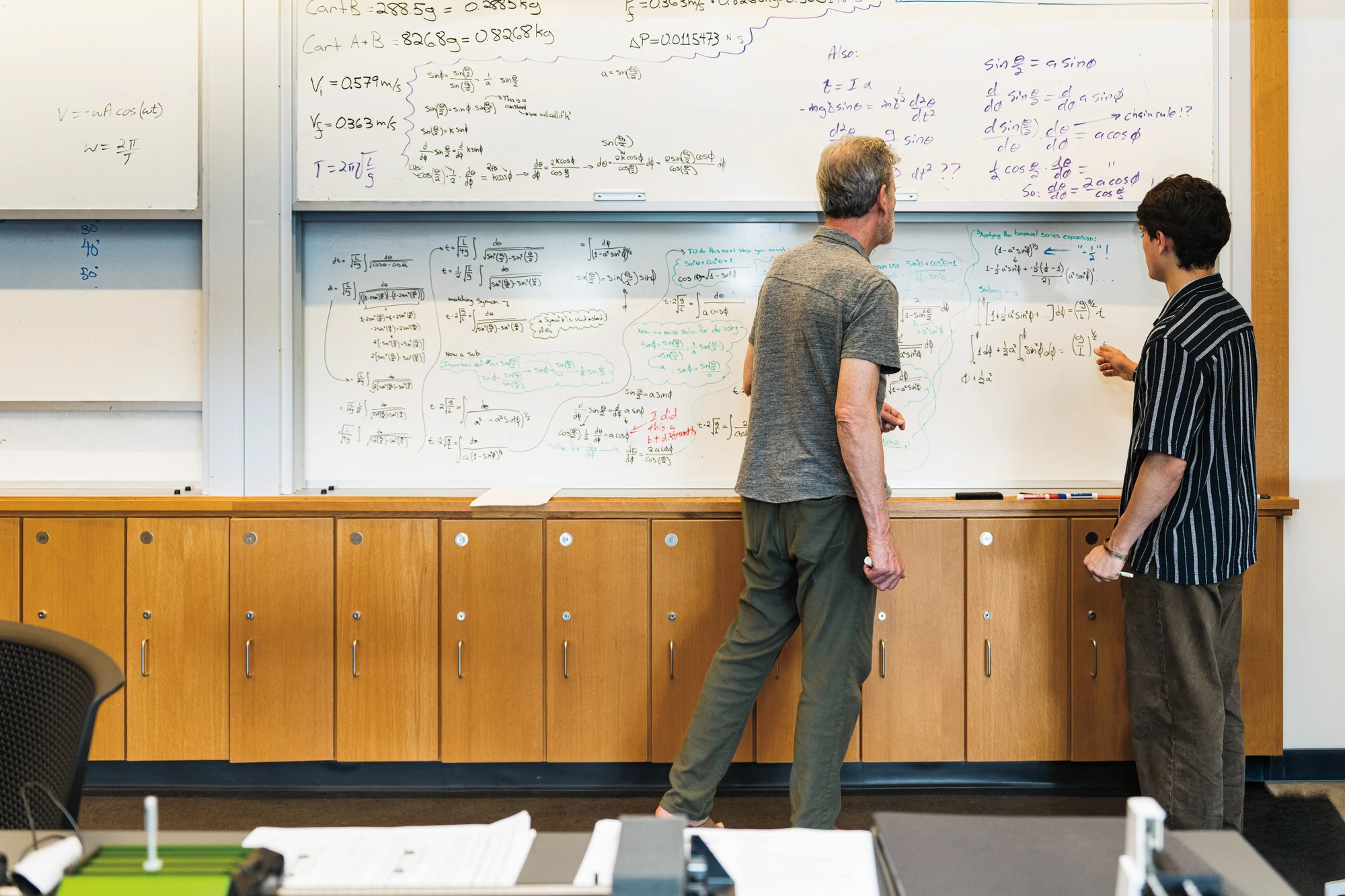 Two men are writing on a white board.