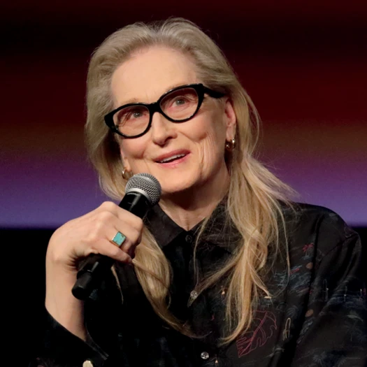 Meryl Streep smiles while speaking into a handheld microphone.