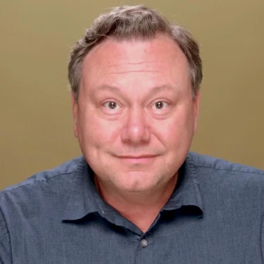 Eddie Gamarra smiles slightly in a headshot against a tan background.