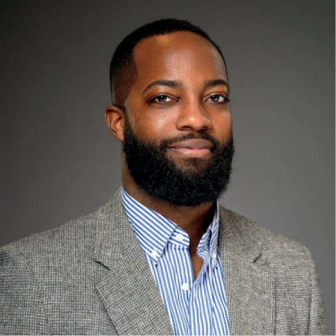 Seth Bynum poses in a gray blazer and striped shirt against a neutral background.