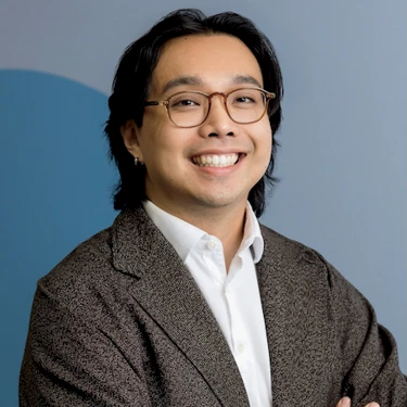 Johnson Lin smiles with his arms crossed, wearing glasses and a dark blazer.