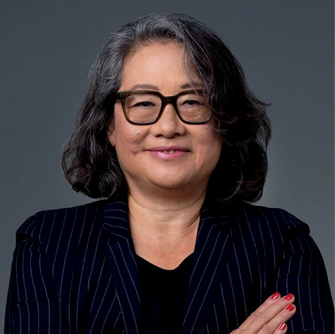 Minerva Tantoco poses with her arms crossed, wearing glasses and a pinstriped blazer.