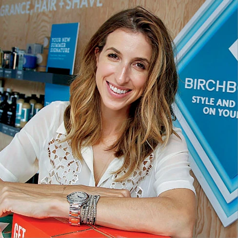 Katia Beauchamp smiles while leaning on a counter in front of a Birchbox display.