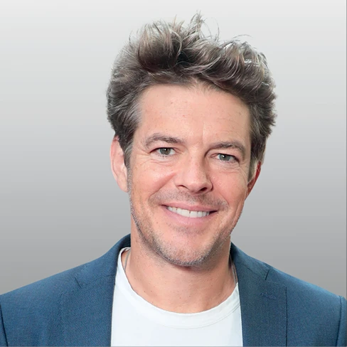 Jason Blum smiles in a blue blazer against a light gray background.